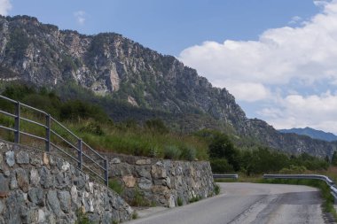 Metal korkulukları, taş duvarları ve bulutlu gökyüzünün altındaki dik orman yamaçları olan dolambaçlı dağ yolu. Alp manzarası araba sürmek, turizm, dağ yolları ve macera kavramları için mükemmel..