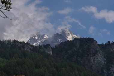 Alp dağlarının karlı sırtı bulutlu gün ışığı altında katmanlı yeşil orman tepelerinin üzerinde. Doğa ve macera temaları için güzel seyahat manzarası.
