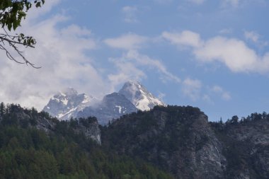 Alp dağlarının karlı sırtı bulutlu gün ışığı altında katmanlı yeşil orman tepelerinin üzerinde. Doğa ve macera temaları için güzel seyahat manzarası.