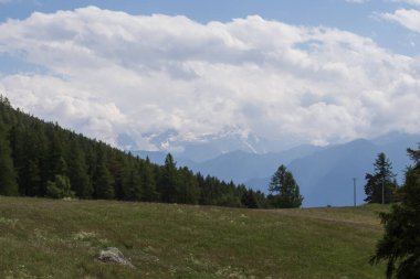 Karla kaplı zirveler, çarpıcı bulutlarla dolu yemyeşil orman yamaçlarının üzerinde duruyor. Seyahat, yürüyüş, irtifa ve manzara temaları için ideal barışçıl bir dağ manzarası..