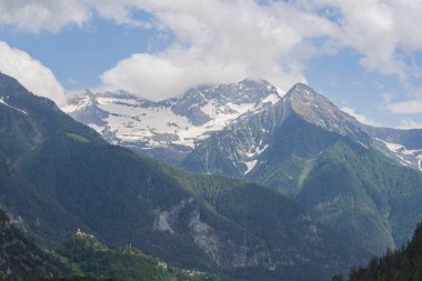 Alp dağlarının karlı sırtı bulutlu gün ışığı altında katmanlı yeşil orman tepelerinin üzerinde. Doğa ve macera temaları için güzel seyahat manzarası.