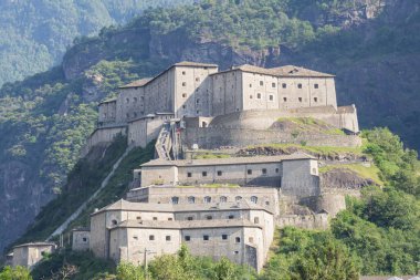 Ormanlı kayalık bir dağlık yamacın üzerindeki tarihi Bard Kalesi. Taş duvarlar ve savunma terasları İtalya 'da kültürel miras olarak bir dönüm noktası oluşturur..