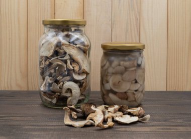 Ahşap masadaki kavanozlarda korunmuş porcini mantarları. Bir kavanoz kurutulmuş, bir kavanoz marine edilmiş, gevşek dilimlenmiş. Kış yemekleri için doğal kırsal hasat deposu.