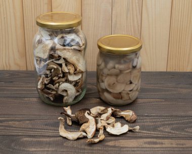 Ahşap masadaki kavanozlarda korunmuş porcini mantarları. Bir kavanoz kurutulmuş, bir kavanoz marine edilmiş, gevşek dilimlenmiş. Kış yemekleri için doğal kırsal hasat deposu.