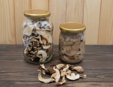Ahşap masadaki kavanozlarda korunmuş porcini mantarları. Bir kavanoz kurutulmuş, bir kavanoz marine edilmiş, gevşek dilimlenmiş. Kış yemekleri için doğal kırsal hasat deposu.