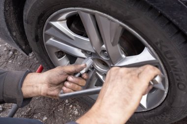 İşçi elleri araba lastiğini değiştirirken ingiliz anahtarıyla tekerlek cıvatalarını sıkıyor. El işi sürecini gösteren otomotiv bakım ve onarım konsepti.