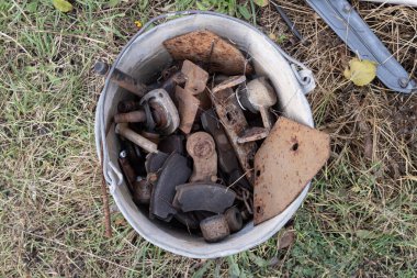 Paslı metal cıvataları ve çimlerin üzerinde kırıntıları olan yaşlı bir kova. Çürümeyi, aşınmayı ve eski makine atıklarını temsil eden endüstriyel geri dönüşüm kavramı.