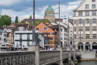 Limmat Nehri köprüsü ve Zürih 'in eski bir kasabası. Uzakta ETH Zürih kubbesi var. İnsanlar, evler ve bulutlu yaz havası, İsviçre.