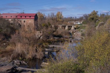Tarihi taş değirmeni, eski taş köprüsü ve sonbahar ağaçları, yansımaları ve doğal dokularıyla çevrili kayalık nehri olan huzurlu kırsal vadi..