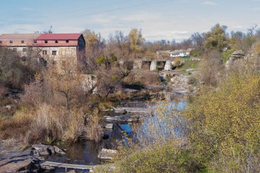 Tarihi taş değirmeni, eski taş köprüsü ve sonbahar ağaçları, yansımaları ve doğal dokularıyla çevrili kayalık nehri olan huzurlu kırsal vadi..