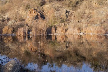 Terk edilmiş granit ocağında sakin bir göl. Kayalık kıyılar ve sonbahar ormanı sessiz sulara yansıyor. Gün batımında huzurlu doğal manzara.