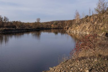 Günbatımında yansıtıcı su ve kayalık uçurumlarla terk edilmiş bölgede sakin granit ocağı gölü.