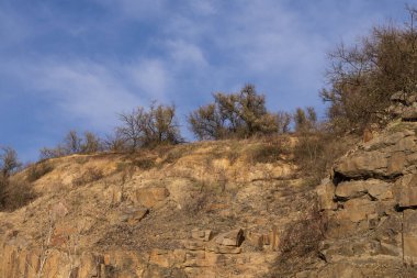 Büyük kaya kayalıkları, katmanlı kaya oluşumları ve kuru sonbahar bitkileriyle Rocky taş ocağı arazisi. Doğa, jeoloji ve çevre temaları için ideal doğal manzara.