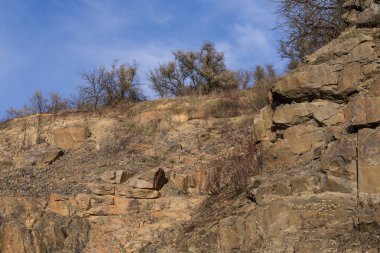 Büyük kaya kayalıkları, katmanlı kaya oluşumları ve kuru sonbahar bitkileriyle Rocky taş ocağı arazisi. Doğa, jeoloji ve çevre temaları için ideal doğal manzara.