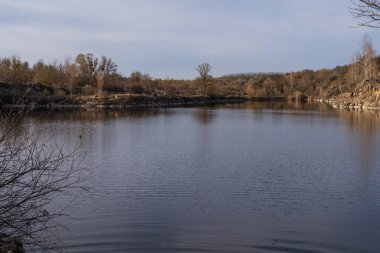 Günbatımında yansıtıcı su ve kayalık uçurumlarla terk edilmiş bölgede sakin granit ocağı gölü.