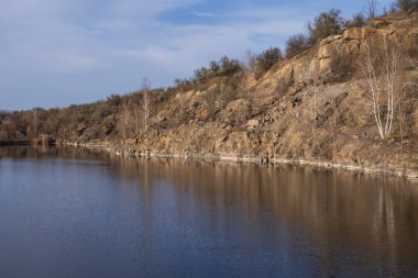 Günbatımında yansıtıcı su ve kayalık uçurumlarla terk edilmiş bölgede sakin granit ocağı gölü.