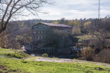 Tuğladan pencereleri ve yıpranmış dış duvarları olan tarihi taştan bir bina. Kuru bitki örtüsü ve doğal manzarayla çevrili eski kırsal mimari.