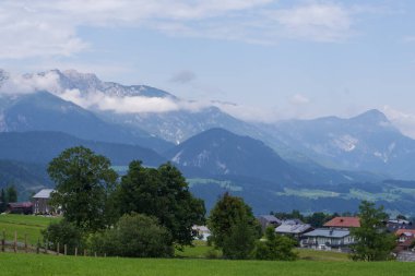 Geniş çayırları, sık orman tepeleri ve köy binaları olan doğal dağ manzarası. Seyahat, doğa ve çevre konuları için ideal sakin kırsal görünüm.
