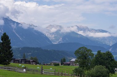 Geniş çayırları, sık orman tepeleri ve köy binaları olan doğal dağ manzarası. Seyahat, doğa ve çevre konuları için ideal sakin kırsal görünüm.