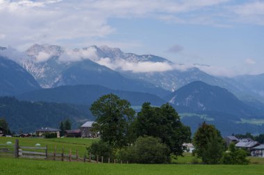 Geniş çayırları, sık orman tepeleri ve köy binaları olan doğal dağ manzarası. Seyahat, doğa ve çevre konuları için ideal sakin kırsal görünüm.