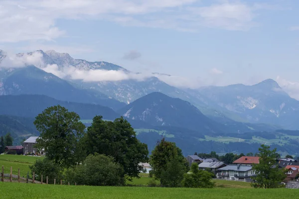 Geniş çayırları, sık orman tepeleri ve köy binaları olan doğal dağ manzarası. Seyahat, doğa ve çevre konuları için ideal sakin kırsal görünüm.