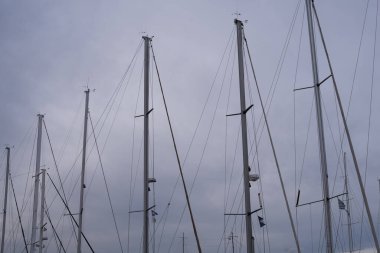 Marina yelkenli direği bulutlu gökyüzüne karşı donatılmış. Dikey çizgiler ve deniz donanımlı asgari deniz manzarası.