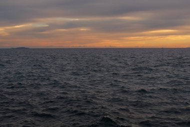 Akşam deniz manzarası, hareketli Ege Denizi dalgalarına altın gün batımı yansımalarını gösteriyor. Atina kıyısı yakınlarındaki sakin doğal manzara dramatik bulutlar ve sıcak ufuklar.