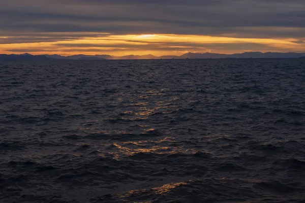 Akşam deniz manzarası, hareketli Ege Denizi dalgalarına altın gün batımı yansımalarını gösteriyor. Atina kıyısı yakınlarındaki sakin doğal manzara dramatik bulutlar ve sıcak ufuklar.