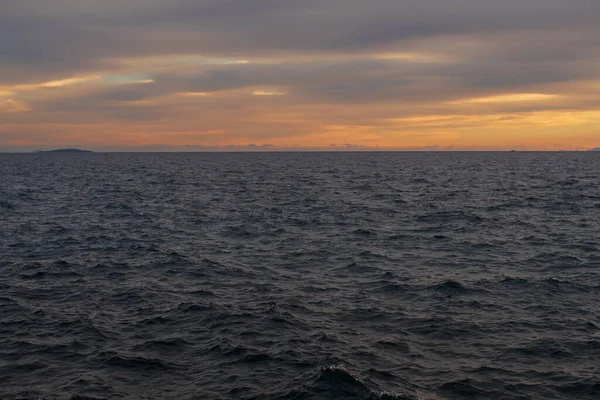 Akşam deniz manzarası, hareketli Ege Denizi dalgalarına altın gün batımı yansımalarını gösteriyor. Atina kıyısı yakınlarındaki sakin doğal manzara dramatik bulutlar ve sıcak ufuklar.