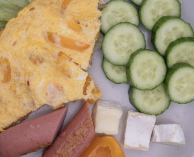 Sağlıklı kahvaltı tabağı omlet, dilimlenmiş sosis, peynir, salatalık ve marul. Basit ev yemekleri, dengeli beslenme ve günlük yiyecek konsepti..