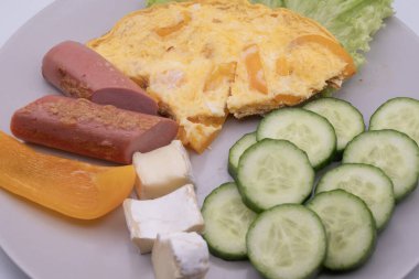 Sağlıklı kahvaltı tabağı omlet, dilimlenmiş sosis, peynir, salatalık ve marul. Basit ev yemekleri, dengeli beslenme ve günlük yiyecek konsepti..