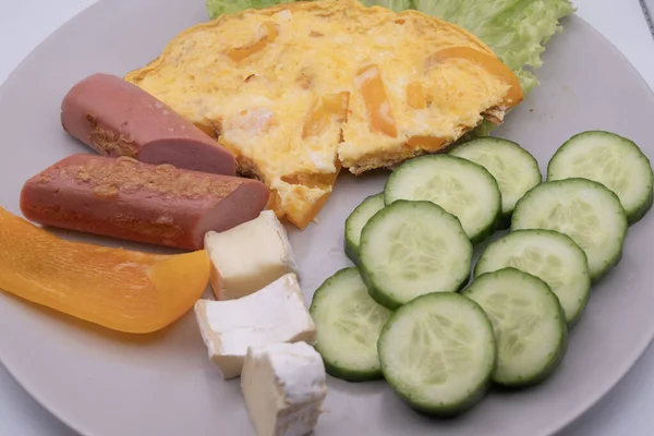 Sağlıklı kahvaltı tabağı omlet, dilimlenmiş sosis, peynir, salatalık ve marul. Basit ev yemekleri, dengeli beslenme ve günlük yiyecek konsepti..