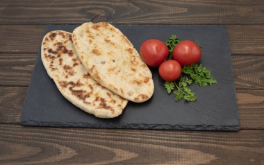 Kızartma ile pişirilen altın ince patates turtaları, taze domates ve maydanozla servis edilen siyah tahta üzerinde.