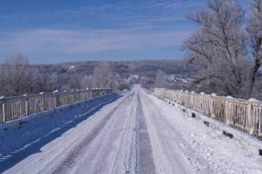 Buzlu kırsal yol buzlu ağaçlar ve parlak mavi gökyüzü ile çevrili. Kış yolculuğu ve soğuk hava konsepti.