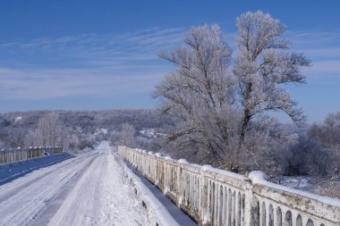 Buzlu kırsal yol buzlu ağaçlar ve parlak mavi gökyüzü ile çevrili. Kış yolculuğu ve soğuk hava konsepti.