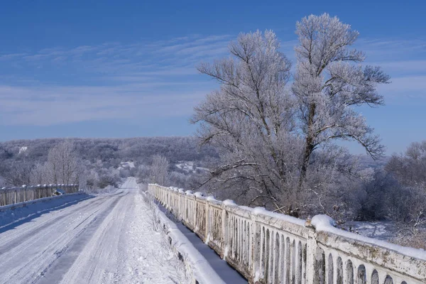 Buzlu kırsal yol buzlu ağaçlar ve parlak mavi gökyüzü ile çevrili. Kış yolculuğu ve soğuk hava konsepti.