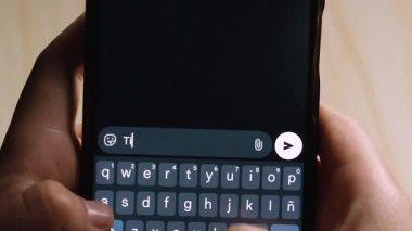 Akıllı telefon mesajlaşma uygulamasında Ti amo 'yu yazarken, koyu bir sohbet arayüzü ve dokunmatik ekran klavyesini kullanımda gösteren ellerin yakın plan görüntüsü.