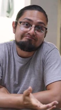 Gözlüklü sıradan bir adam rahat bir ortamda otururken neşeli ve kendinden emin bir ifade takınıyor..