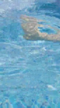 Dalgalanan mavi havuz suyunun altında süzülen insan bacağının bulanık görüntüsü sakin ve soyut bir su manzarası yaratıyor..