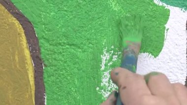 Boya fırçası kullanarak dokulu bir duvara kalın yeşil boya süren bir sanatçının elinin yakın çekimi. Kentsel sanat, yaratıcılık ve ev geliştirme kavramı.