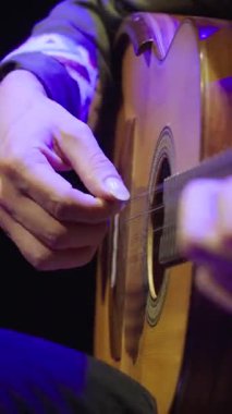 Dikey yakın plan, Kolombiyalı bir enstrüman olan Tiple 'ı çalan bir müzisyenin sağ eline odaklanıyor. Resim, parmak tekniği için kullanılan uzun ve bakımlı tırnakları vurgular..