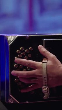 Koyu mavi bir bandoneonun düğmelerini kullanan bir müzisyenin elinin dikey yakın çekimi. Görüntü enstrümanın karmaşık körüklerini ve köşedeki klasik lir amblemini vurgular..