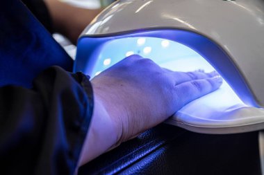 Masadaki çiviler için güzel kadın elleri ve lamba. Manikür tırnaklı bir kadın. Güzellik salonunda jöle lambasında.