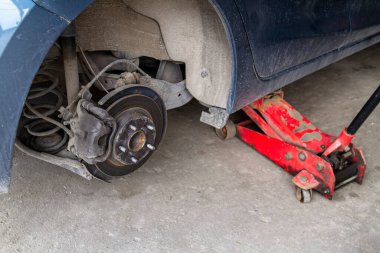 Bir arabanın tekerleklerini değiştirirken, Jack cesedi yüksek pozisyonda tutar. Tekerleksiz araba ve hidrolik kaldırma, lastik değişimi için bekliyor..