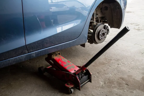 Replacing wheels on a car, jack holds the body in raised position. Car without wheel and lift up by hydraulic, waiting for tire replacement.