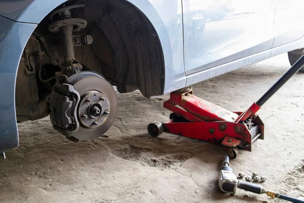 Replacing wheels on a car, jack holds the body in raised position. Car without wheel and lift up by hydraulic, waiting for tire replacement. Pneumatic wrench lies on the asphalt.