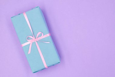 Mor arka planda pembe kurdeleli mavi bir Noel ya da yeni yıl hediyesi kutusu