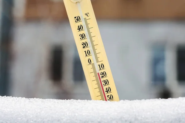 雪の中の温度計は 多階建ての建物の背景に非常に低い温度を示しています 氷点下12度 天気予報の概念 — ストック写真