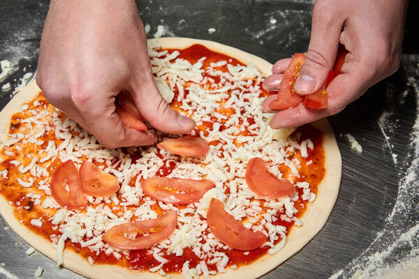The chef lays out tomatoes while making pizza