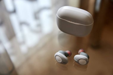 Beyaz kablosuz kulaklıklar ve cam bir yüzeyde kapalı şarj kutusu.